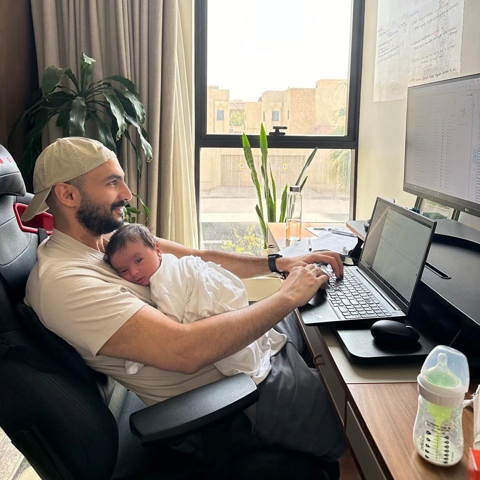 A man working at a laptop while holding a baby.